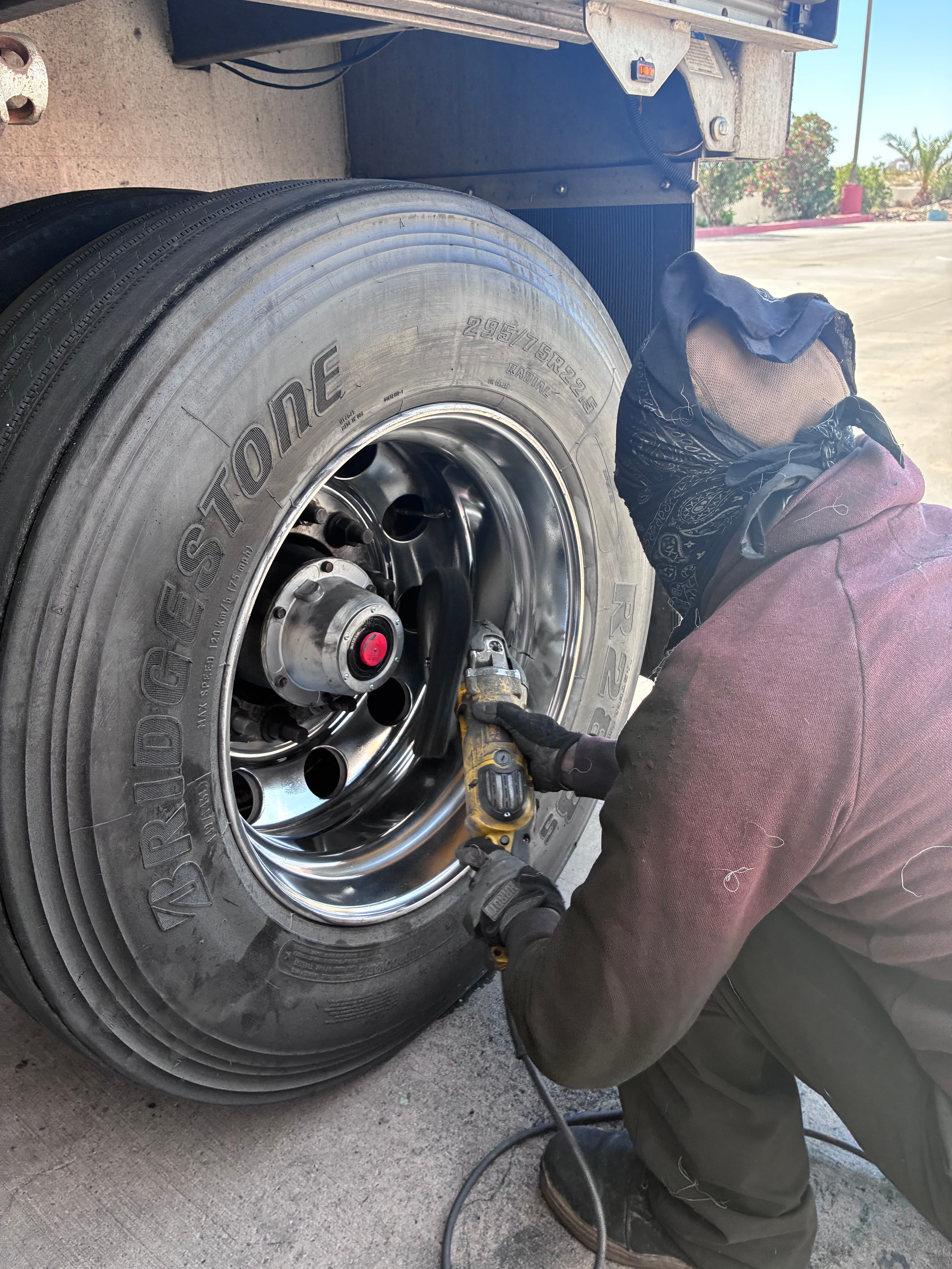 Worker using a power tool on the chrome rim of a large Bridgestone truck tire.