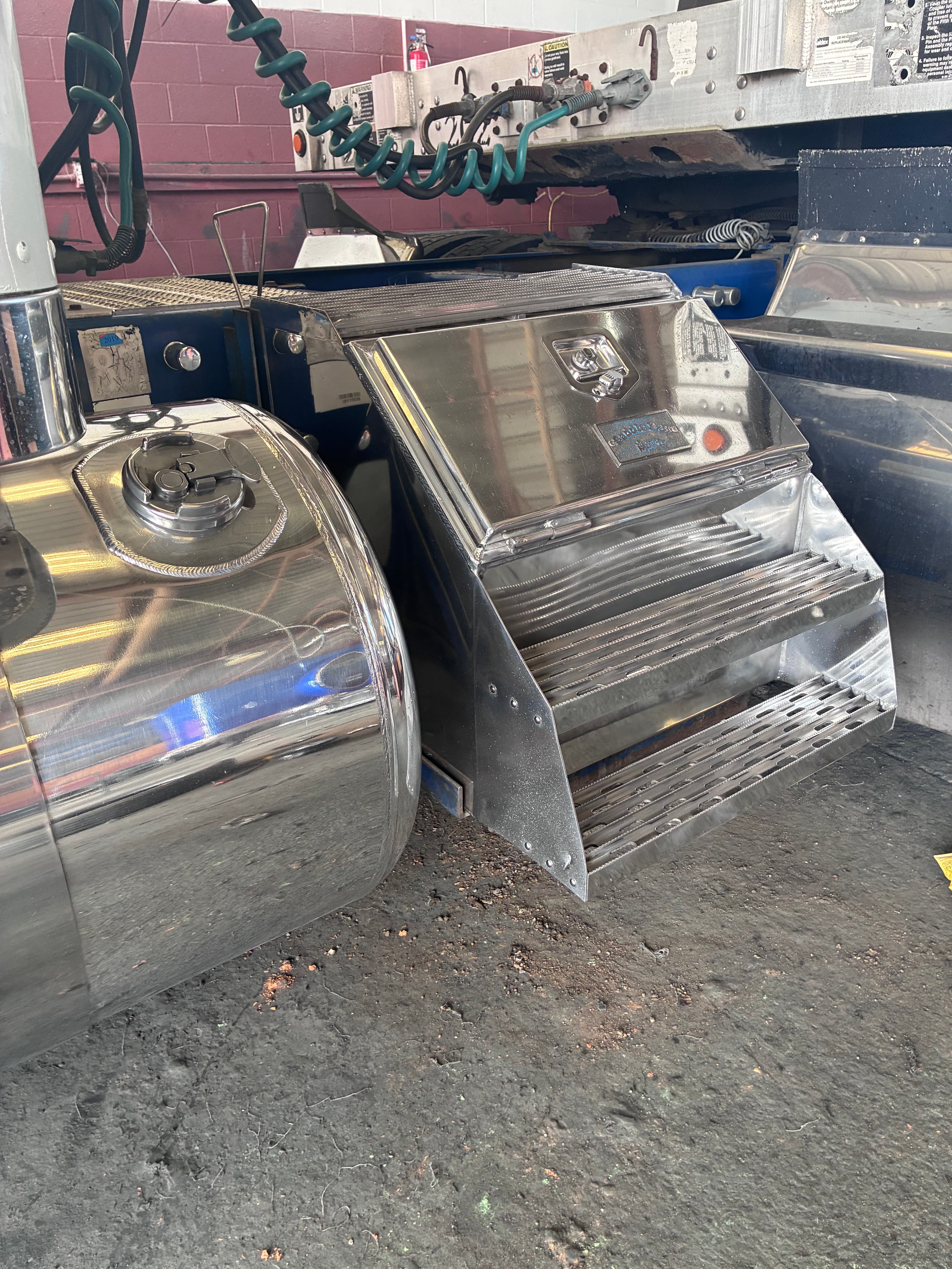 Polished chrome fuel tank and storage box on a semi-truck with coiled air hoses.