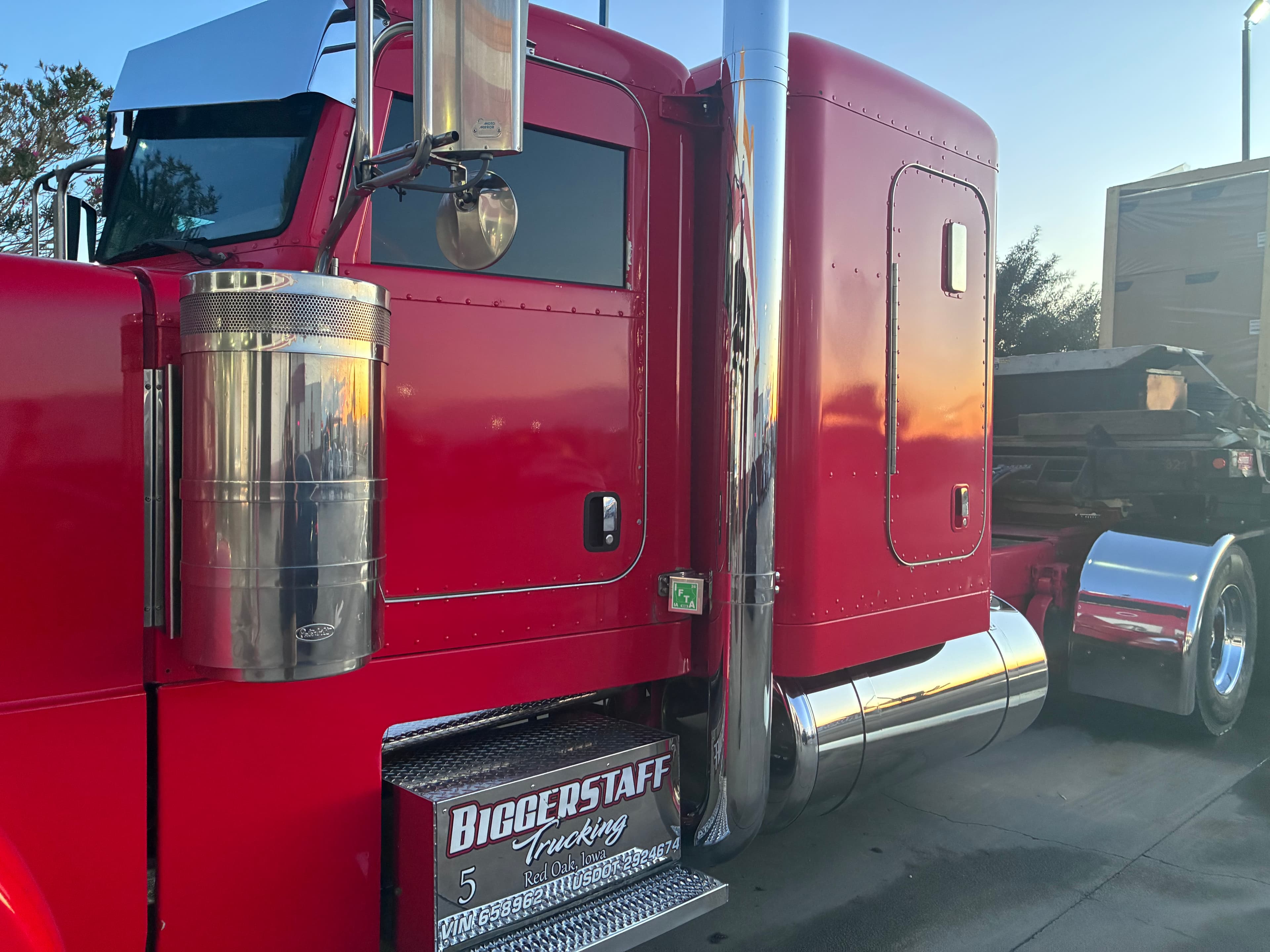 Red semi truck with chrome accents and Biggerstaff Trucking logo reflecting a golden sunset.