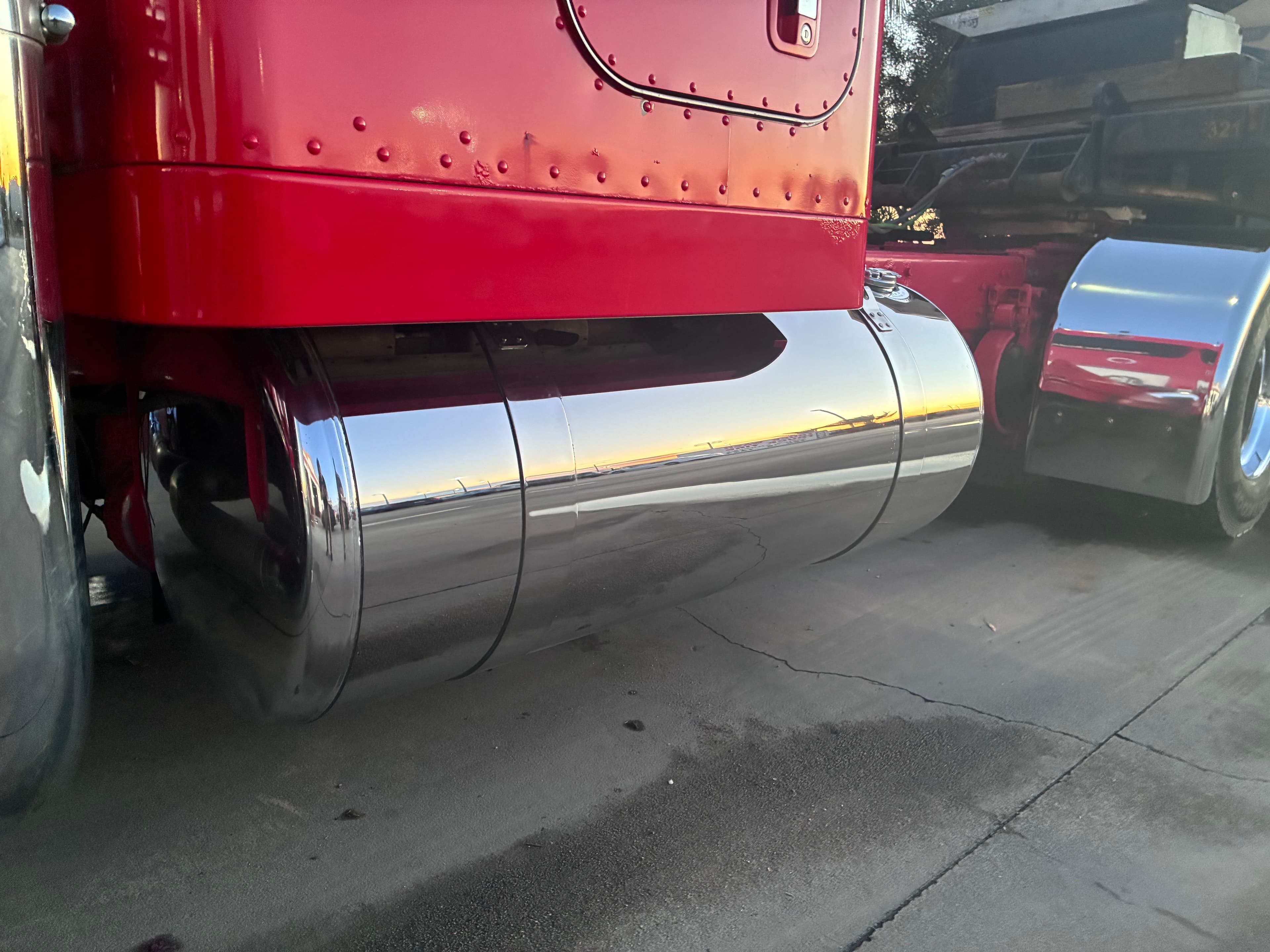 Close-up of a red semi-truck's shiny chrome fuel tank reflecting the horizon at dusk.